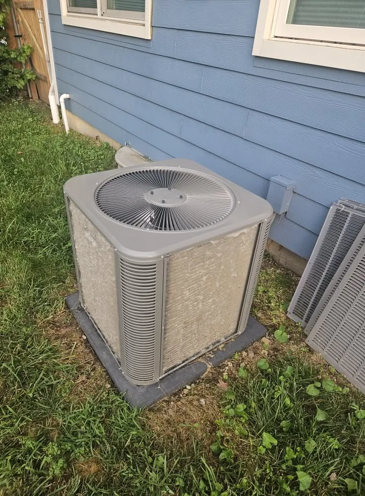 Outdoor air conditioner condenser beside a blue house