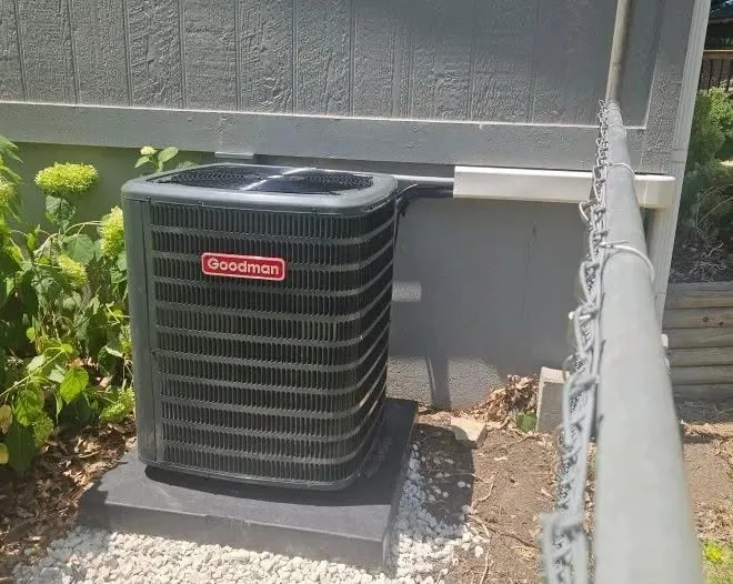 Goodman outdoor condenser on a pad beside a home