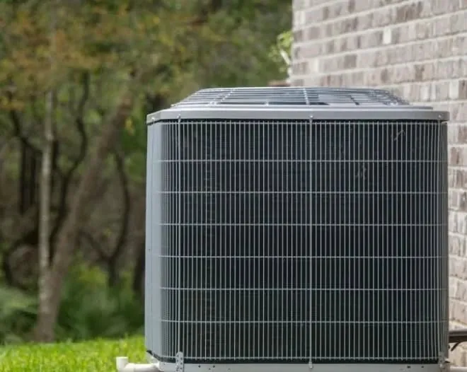 Large outdoor condenser unit with a wire guard beside a brick wall