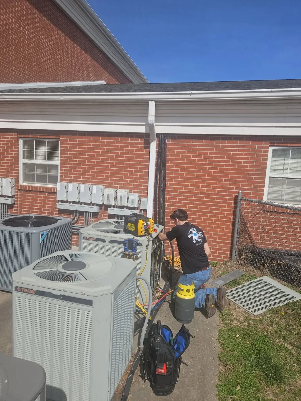 Technician working at outdoor condensers beside a brick home
